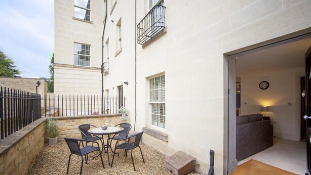 Un pequeño patio exterior con una mesa y sillas, un muro de piedra y la entrada de un edificio.