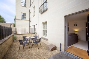 Eine kleine Außenpatio mit Tisch und Stühlen, eine Steinmauer und ein Gebäudeeingang.