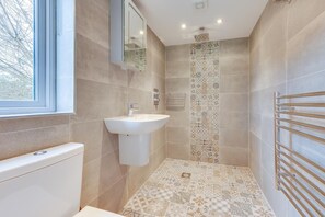 A bathroom with a white sink, a mirror, a shower with a tiled wall, and a towel rack. - 1 Bed in Beckley (oc-rh1151) (Beckley)
