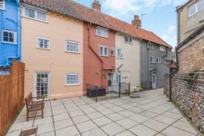 A narrow street with terraced houses, a wooden fence, and a bench.