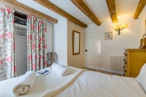 Un dormitorio con cama, cabecera de madera, una silla, armario, espejo y una lámpara de pared.