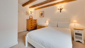 A bedroom with a large bed, wooden dresser, two bedside tables with lamps, and a ceiling with exposed beams.