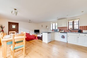A spacious living area with a dining table, red sofa, and a kitchen with white cabinets and a washing machine. - 2 Bed in Benenden (oc-cb540) (Benenden)