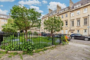 A residential street with a row of terraced houses, a black metal fence, and a garden with various plants. - 2 Bed in Bath (oc-bhr31) (Bath)