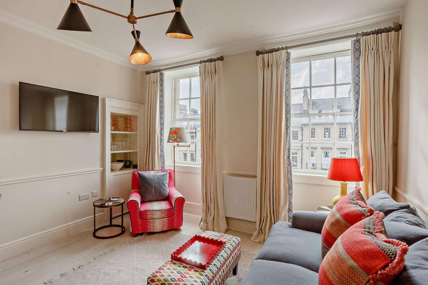 A living room with a red armchair, grey sofa, and a red lamp on a side table.