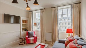 Un salon avec un fauteuil rouge, un canapé gris et une lampe rouge posée sur une table d’appoint.