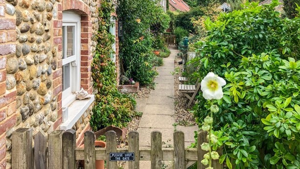 A narrow pathway flanked by stone and brick buildings, leading to a gate with a sign that reads "PLEASE SHUT THE GATE." - 1 Bed in Stiffkey (oc-1642) (Stiffkey)