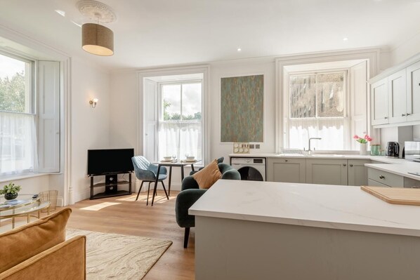 Una cocina moderna con una isla central, un comedor con televisor y un amplio ventanal que proporciona luz natural.