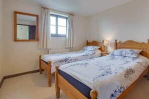 A bedroom with two wooden beds, a window with curtains, a mirror, and a bedside lamp.