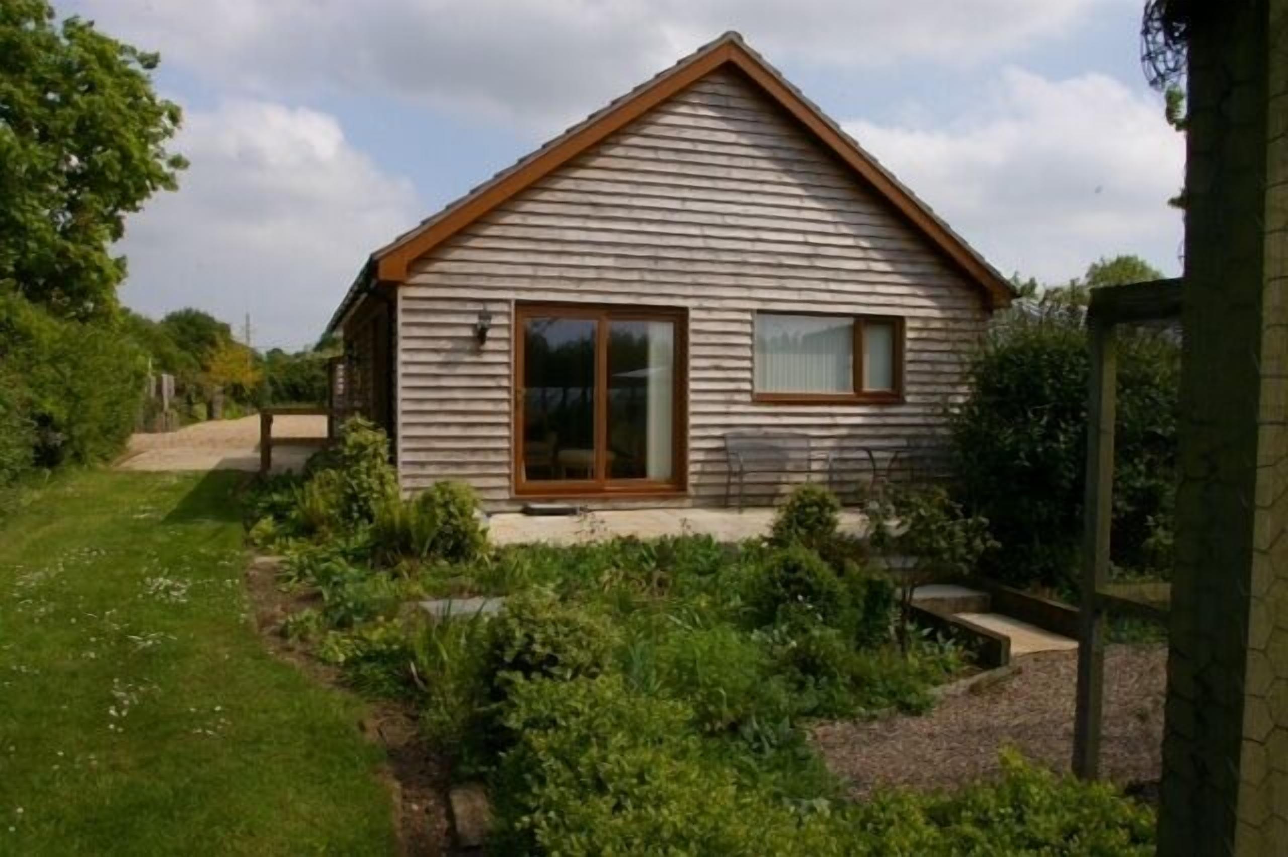 Une maison en bois d’un seul étage, dotée d’un toit à pignon, d’un porche à l’avant et d’un petit jardin.