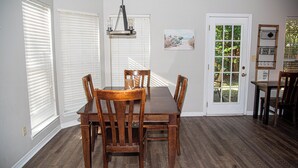 Een eethoek met een houten tafel en stoelen, een kroonluchter en een deur naar buiten.