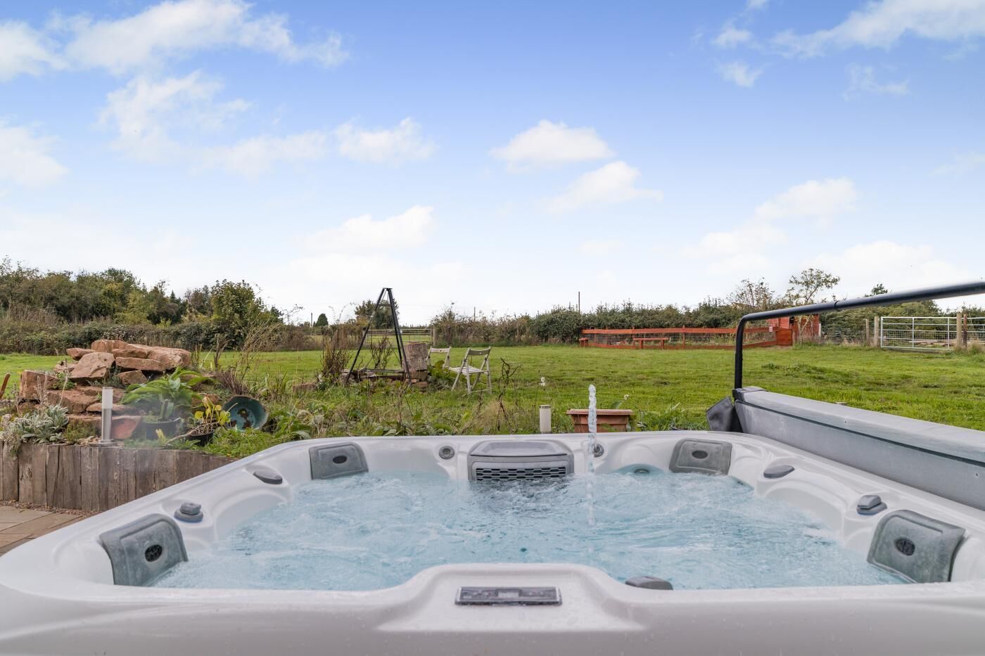 A hot tub in a backyard with a grassy field and a wooden fence in the background.