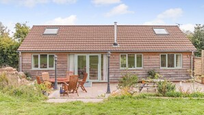 Een houten huis met een pannendak, twee dakramen en een terras met tuinmeubilair.