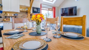 Een eettafel gedekt met borden, glazen en een bloevas, met een keuken en zithoek op de achtergrond.