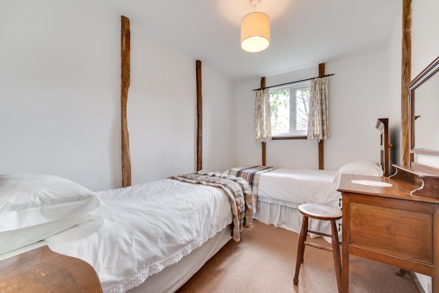 A bedroom with two single beds, a wooden dresser, a mirror, and a window with curtains.