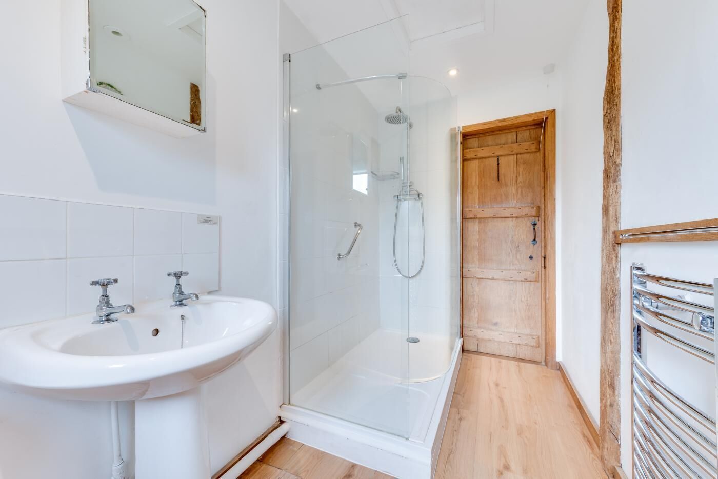 Une salle de bain moderne avec une douche à parois de verre, un lavabo blanc et une porte en bois.