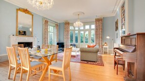 A spacious living room with a dining area, a fireplace, a piano, and large windows. - 2 Bed in Binham (oc-1477) (Binham)