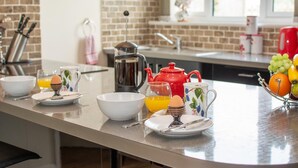Une cuisine avec un mur en briques, une machine à café, une théière rouge et un panier de fruits.