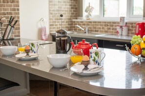 Ett kök med en tegelvägg, en kaffebryggare, en röd tekanna och en fruktskål.
