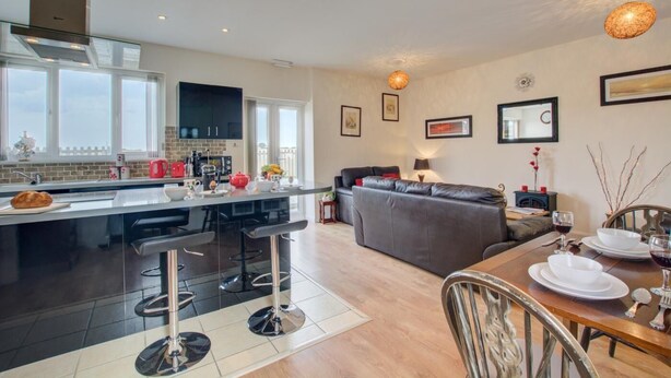 Une cuisine moderne avec un îlot central, un coin repas avec une table et des chaises, un canapé et un balcon avec vue.