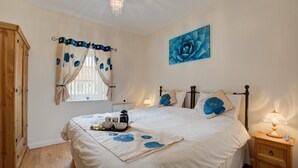 Une chambre à coucher avec un lit, des tables de chevet, une fenêtre avec des rideaux, un tableau au mur et un lustre.