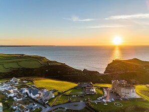 An aerial view of a coastal village with a prominent building, a parking area, and fields. - 3 Bed in Tintagel (oc-e32938) (Tintagel)