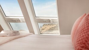 A bed with a view of a coastal landscape through a window. - 3 Bed in Tintagel (oc-e32938) (Tintagel)