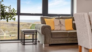 A room with a large window, a grey sofa with yellow cushions, a small table, and a plant. - 3 Bed in Tintagel (oc-e32938) (Tintagel)