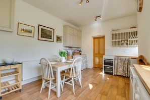 A kitchen with wooden cabinets, a dining table with chairs, a radiator, and a wooden floor.