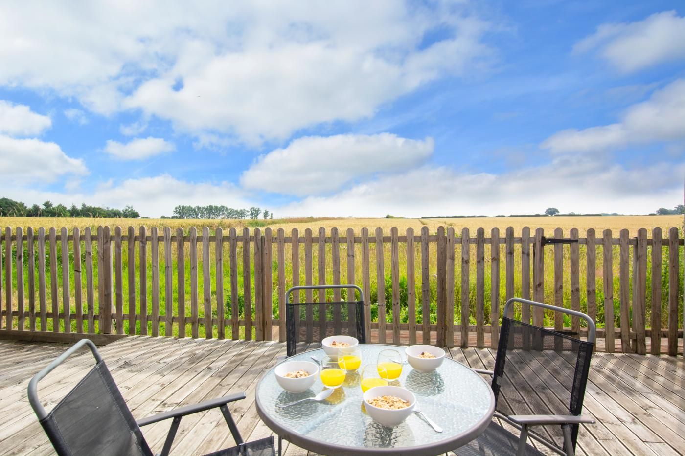 A deck with a table set for breakfast, overlooking a field.