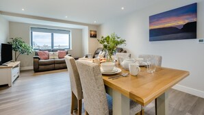 Een moderne woonkamer met een bank, een eettafel met witte borden en kopjes, en een groot raam met uitzicht op de stad.