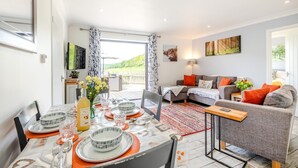 Ein modernes Wohnzimmer mit einer Couch, einem Esstisch für vier Personen und Blick auf eine Terrasse.