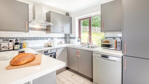Eine moderne Küche mit grauen Schränken, einem Backofen, einem Geschirrspüler und einem Fenster mit Blick ins Freie.