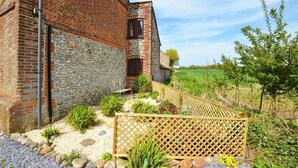 A rustic brick building with a stone wall, a wooden fence, and a gravel pathway leading to a bench. - 2 Bed in Bodham (oc-1660) (Bodham)