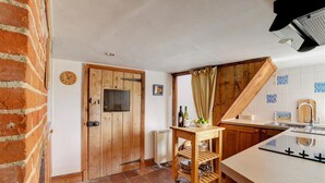 A kitchen with a wooden door, a small table with bottles and fruits, and a tiled backsplash. - 2 Bed in Bodham (oc-1660) (Bodham)