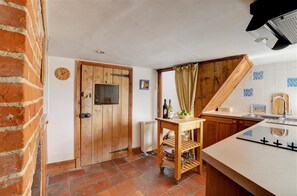 Eine Küche mit einer Holztür, einem kleinen Tisch mit Flaschen und Früchten sowie einer gefliesten Rückwand.
