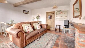 A cozy living room with a brown leather sofa, a wooden door, a small table, and a brick fireplace. - 2 Bed in Bodham (oc-1660) (Bodham)