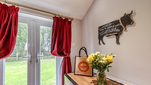 A room with a sliding glass door, a wooden counter, a vase with flowers, a wall-mounted cow decoration, and a red curtain. - 1 Bed in Llandeloy (oc-c32808) (Llandeloy)