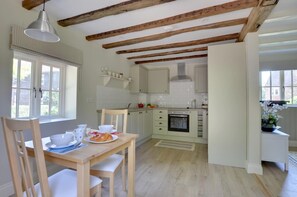 A kitchen with wooden beams, a dining table with chairs, and a window with a view.