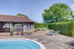 Zona junto a la piscina con terraza de madera, un espacio de estar cubierto y un seto.