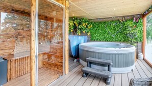 A wooden deck with a hot tub, a glass-enclosed sauna, and a wall of green foliage. - 1 Bed in Horton (oc-b32802) (Horton)
