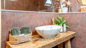 A bathroom with a marble sink, a wooden vanity, a woven basket with towels, and a mirror reflecting a plant and candles. - 1 Bed in Horton (oc-b32802) (Horton)