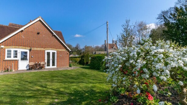 Une maison en briques avec une porte et des fenêtres blanches, une pelouse et un arbuste en fleurs.