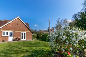 Une maison en briques avec une porte et des fenêtres blanches, une pelouse et un arbuste en fleurs.