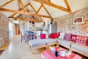 A cozy interior with exposed wooden beams, a stone wall, a dining area with a polka dot tablecloth, and a sofa with colorful pillows. - 2 Bed in Briston (oc-1551) (Briston)