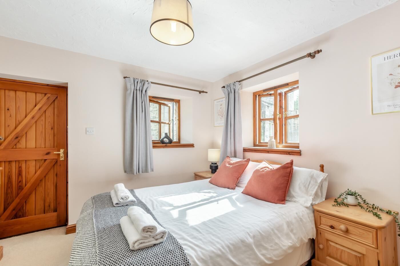 A bedroom with a large bed, two bedside tables, a wooden wardrobe, and two windows with curtains.
