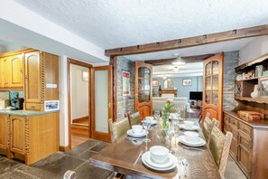 Un coin repas avec une table en bois dressée pour quatre personnes, bordé d’armoires en bois et d’un mur en pierre.
