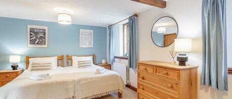 A bedroom with a double bed, wooden headboard, bedside tables with lamps, a dresser, and artwork on the walls.