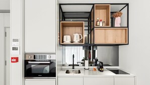 A compact kitchen with a built-in oven, a coffee maker, and a sink. There are wooden shelves above the counter holding kitchen essentials. - GuestReady - Alma Invicta 'Ribeira I' (Porto)