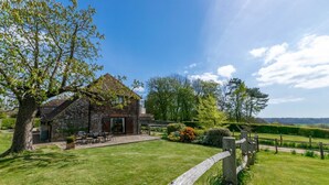 Ein rustikales Steinhaus mit Terrasse und Außenbestuhlung, umgeben von einer gepflegten Rasenfläche und einem Garten.